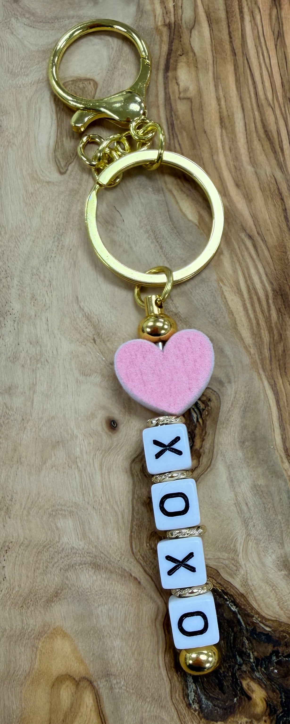 Gold Keychain with 'XOXO' letter beads and pink heart bead on a wooden surface