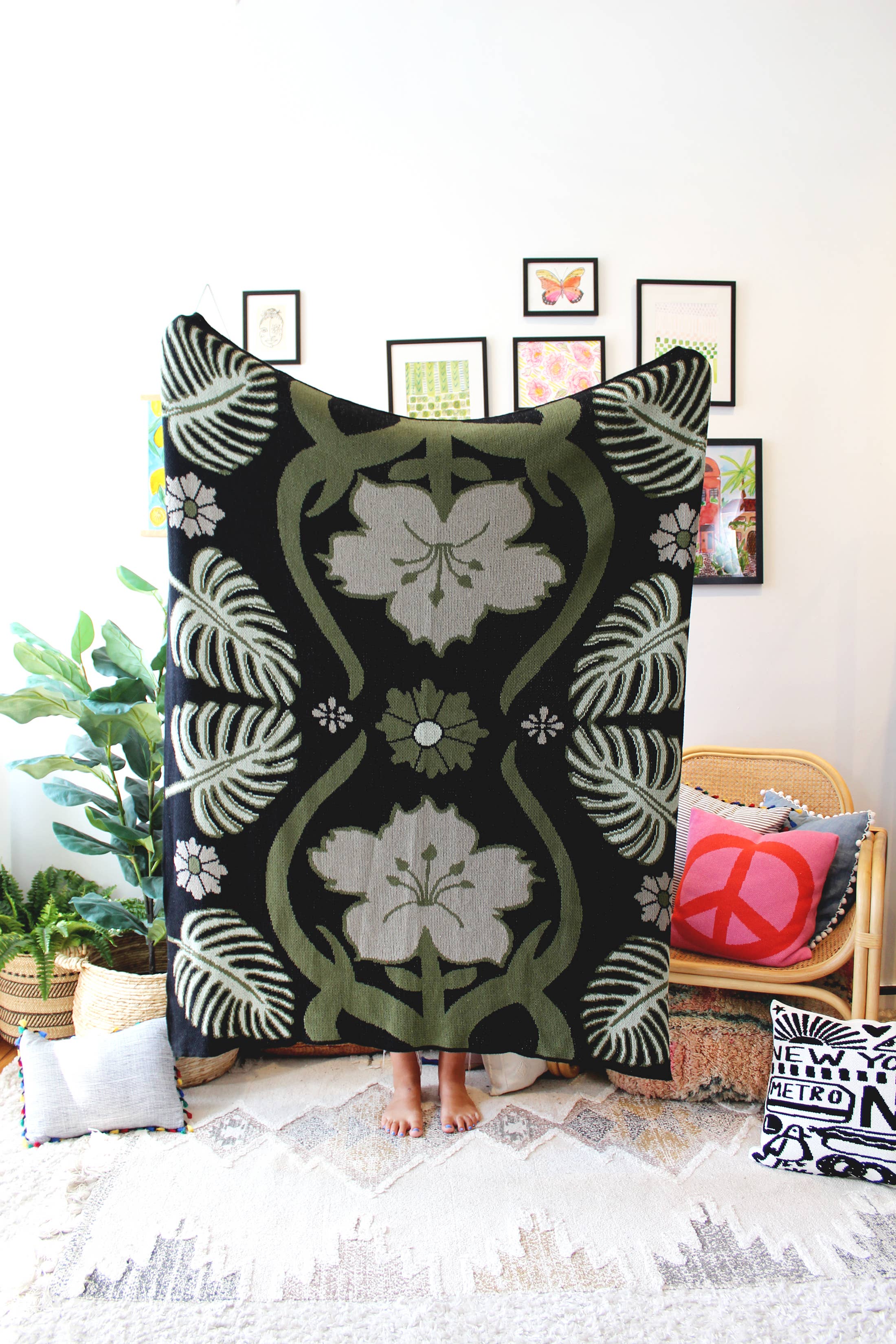 A knit blanket with a geometric pattern featuring floral-like designs in beige, black, and green, displayed over a wooden chair in a room with various decor.