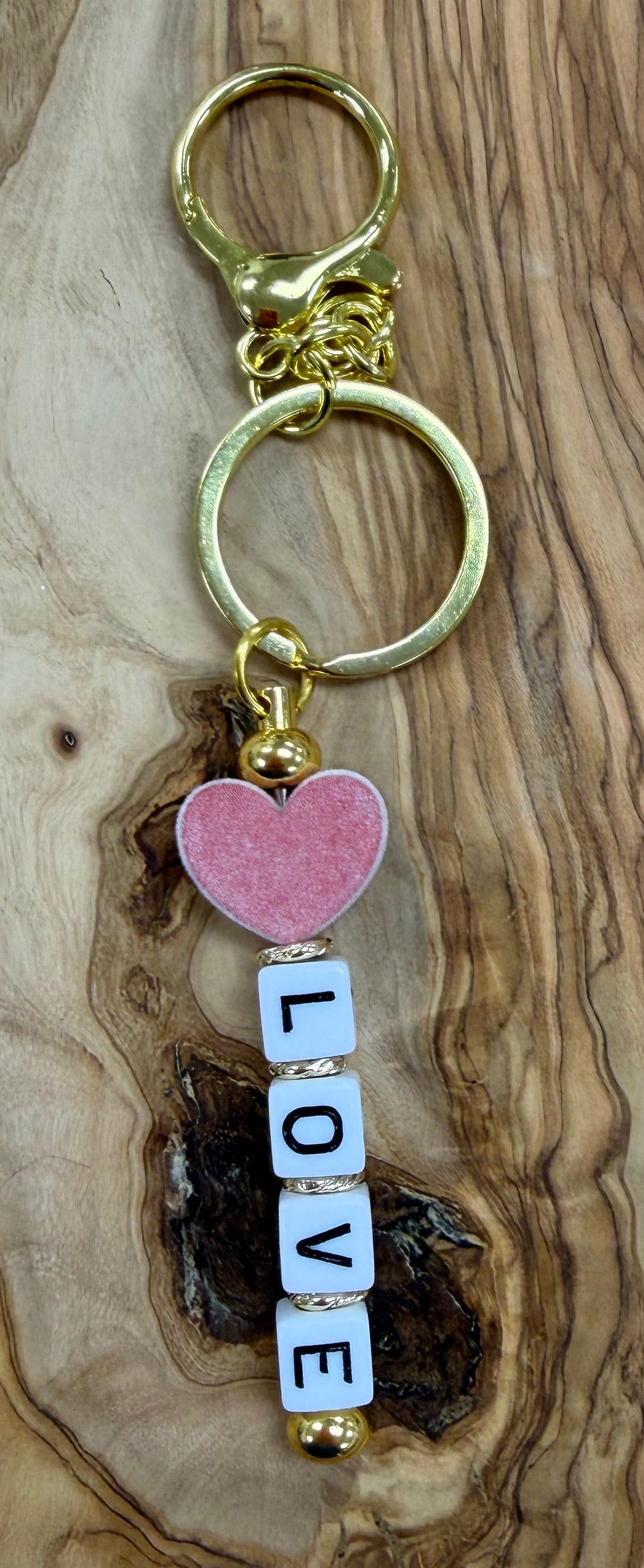 Gold Keychain with 'LOVE' letter beads and a pink heart bead on a wooden surface