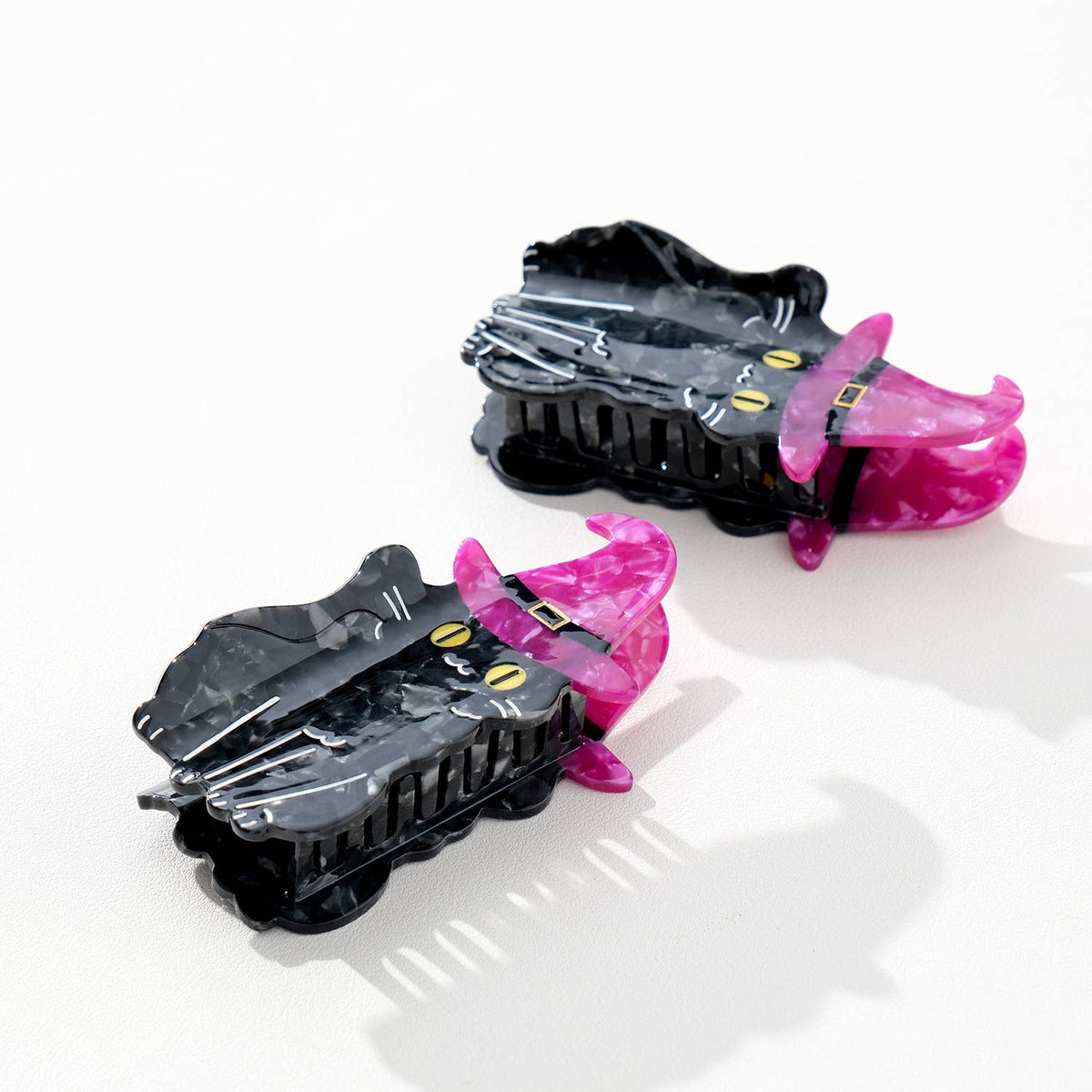 Two black cat-shaped hair clips with purple witch hats on a white background
