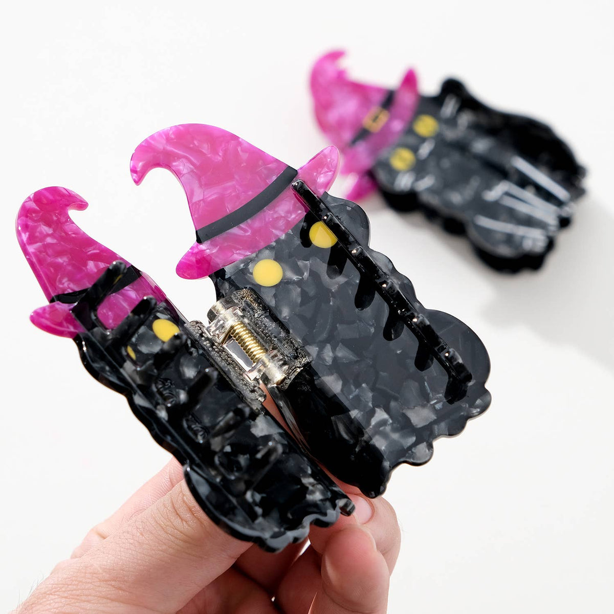 Black cat and purple witch hat hair clip held by a hand on a white background