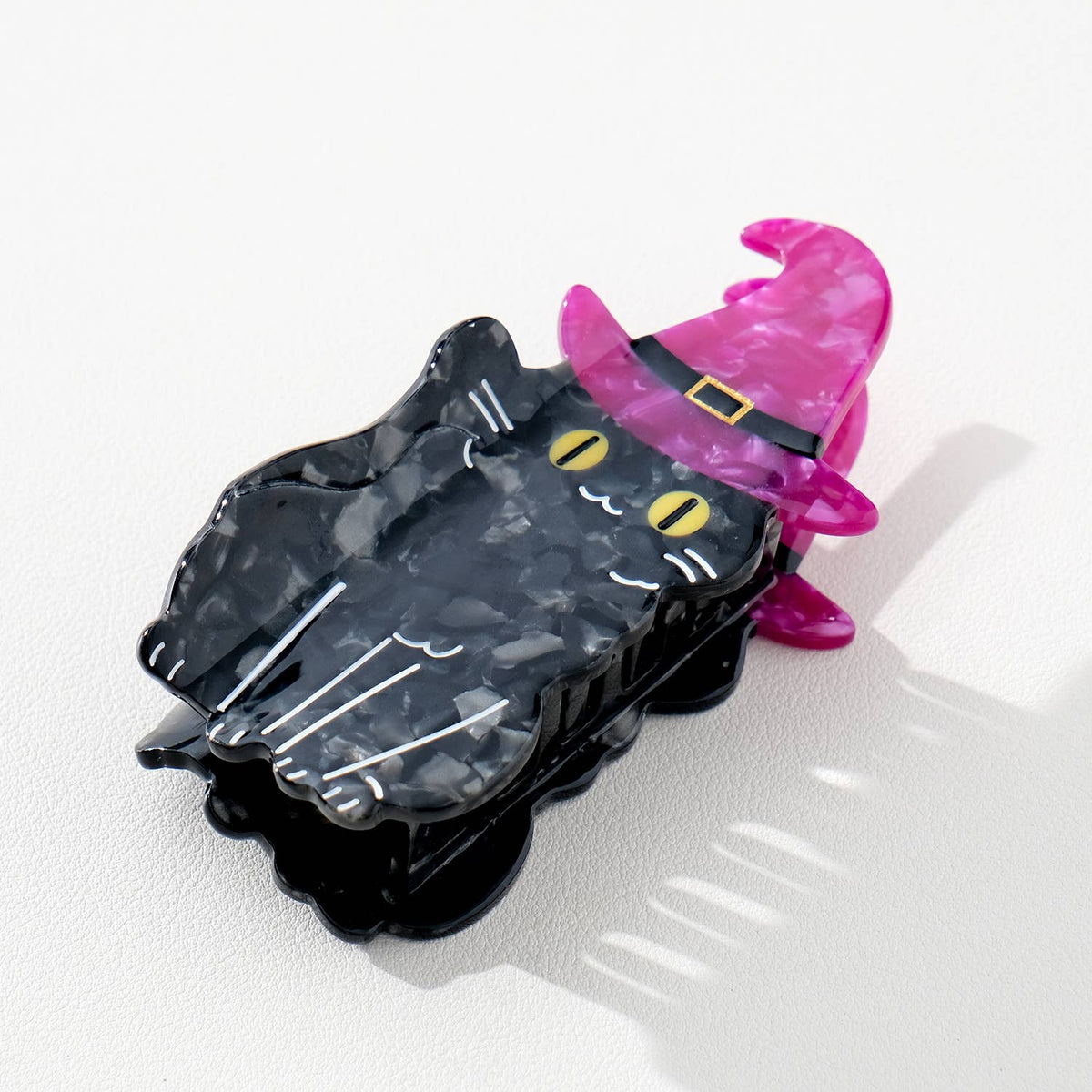Black cat-shaped hairclip with a purple witch hat on a white surface