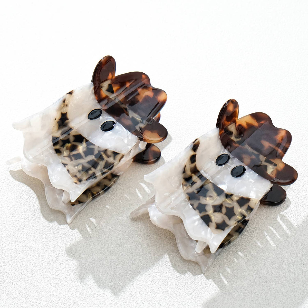 Two ghost-shaped hair clips with tortoiseshell cowbory scarf and hat accents on a white background
