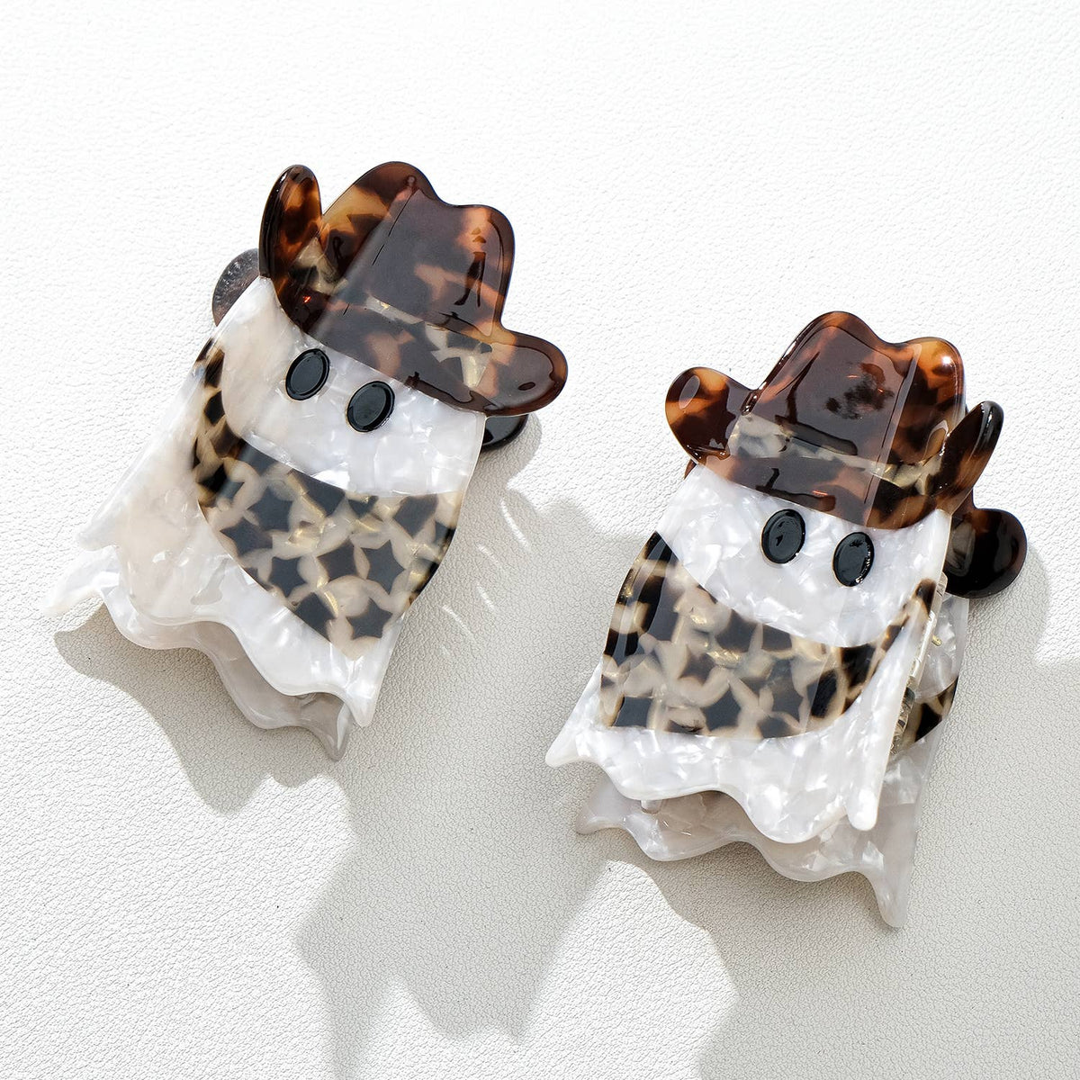 Two ghost-shaped hair clips with tortoiseshell cowbory scarf and hat accents on a white background