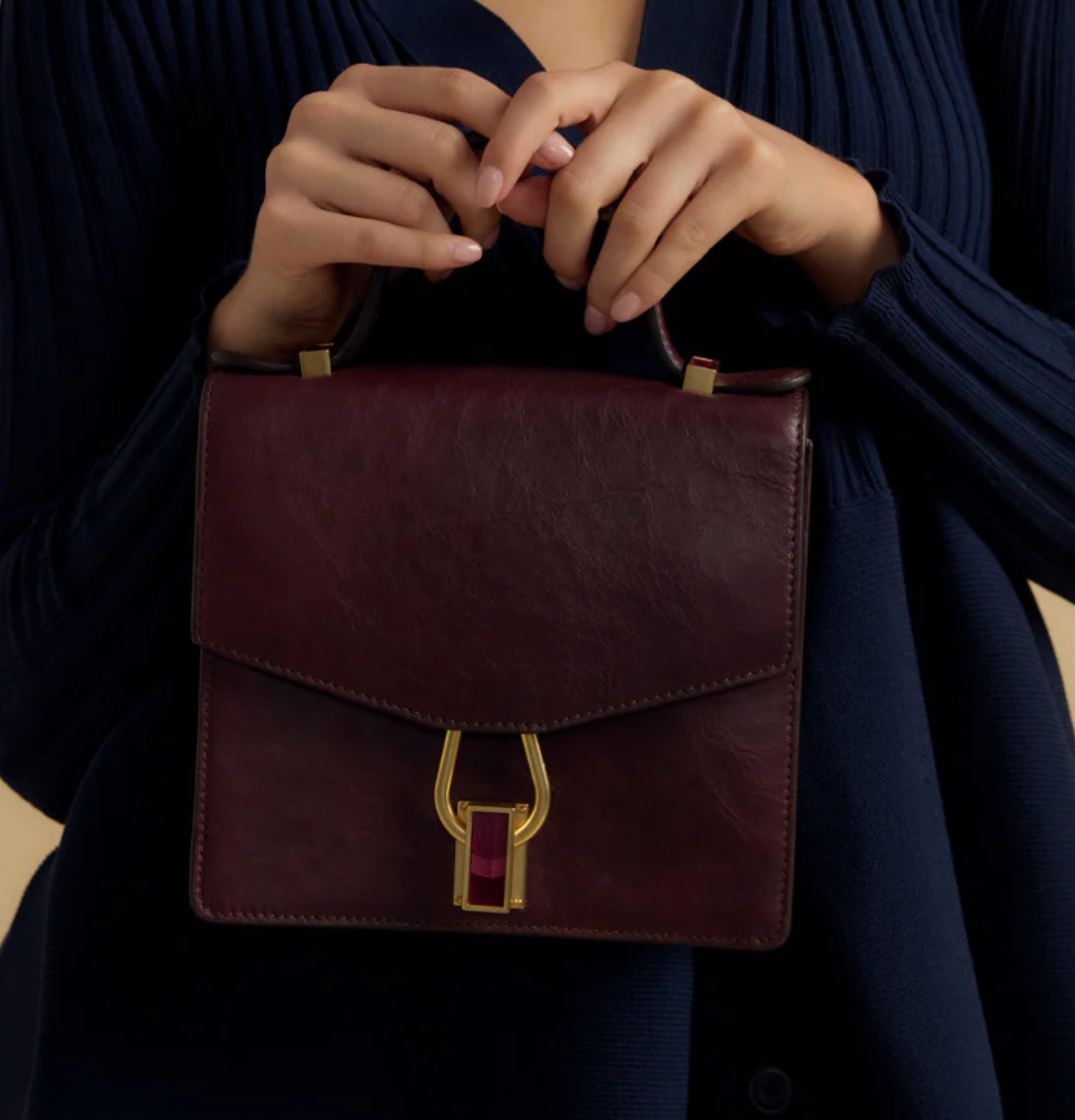 Alternate shot of woman in dark blue dress holding a brown leather handbag with gold clasp featuring maroon feather inlay