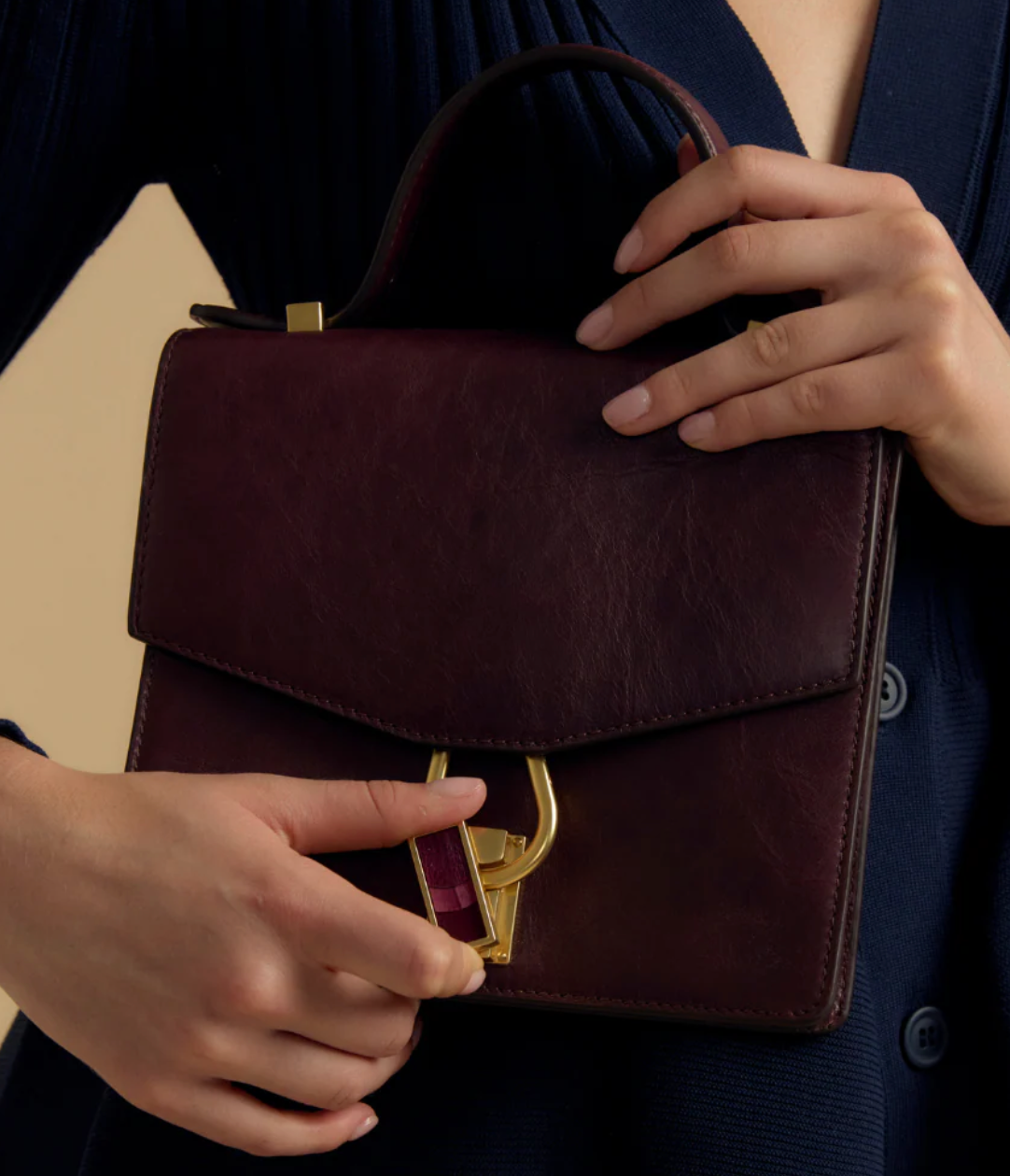 Woman in a dark blue dress modeling a brown leather handbag with gold clasp featuring maroon feather inlay