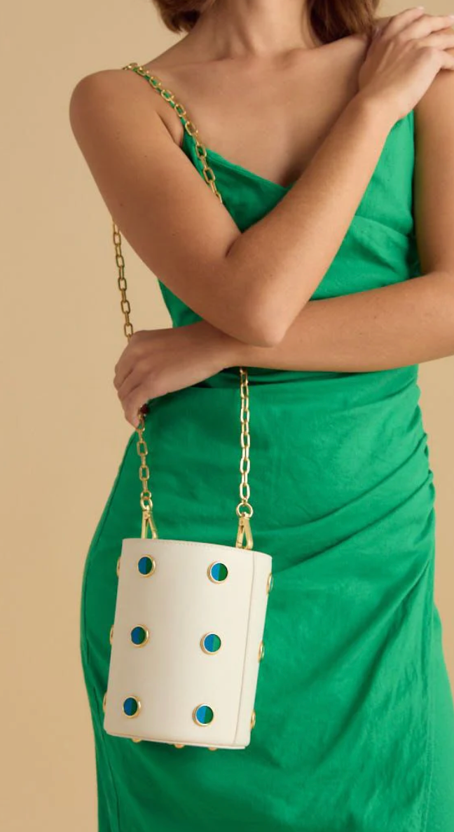 Woman in a green dress modeling a white leather bucket bag with blue and green feather polka dot inlay and gold chain shoulder strap