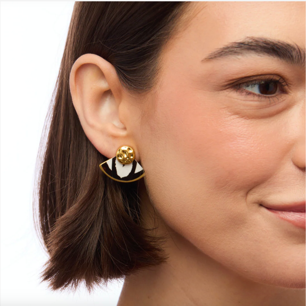 Close-up of a woman wearing a gold earring with a black and white feather inlay against a white background
