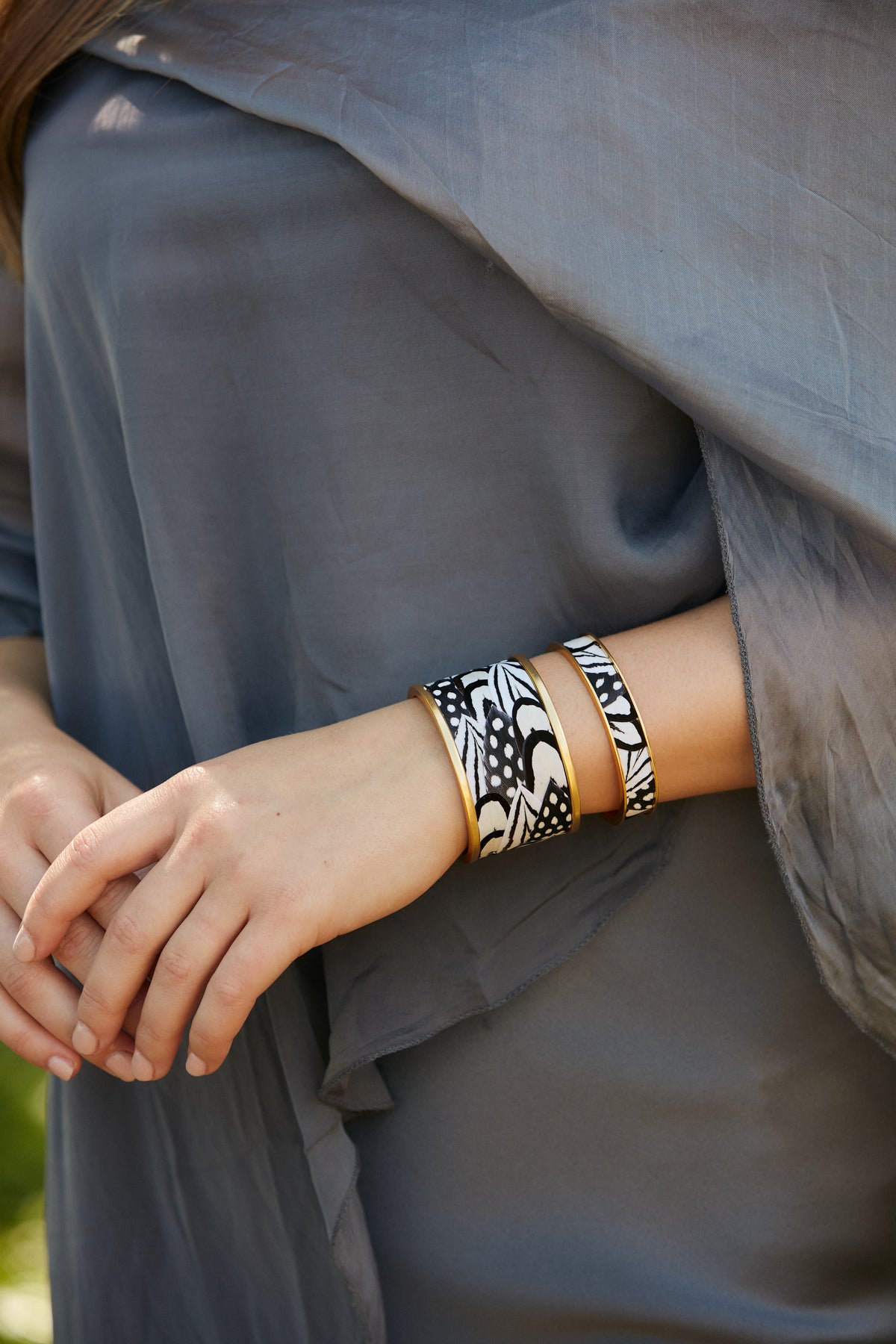 Close-up of a woman in a gray dress modeling a gold cuff with black and white feather inlay