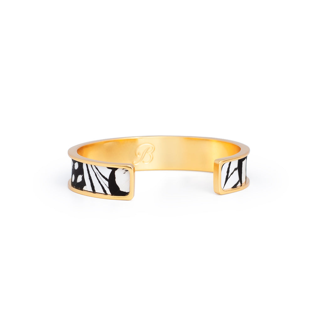 Brackish logo visible on reverse side of gold cuff with black and white feather inlay on a white background