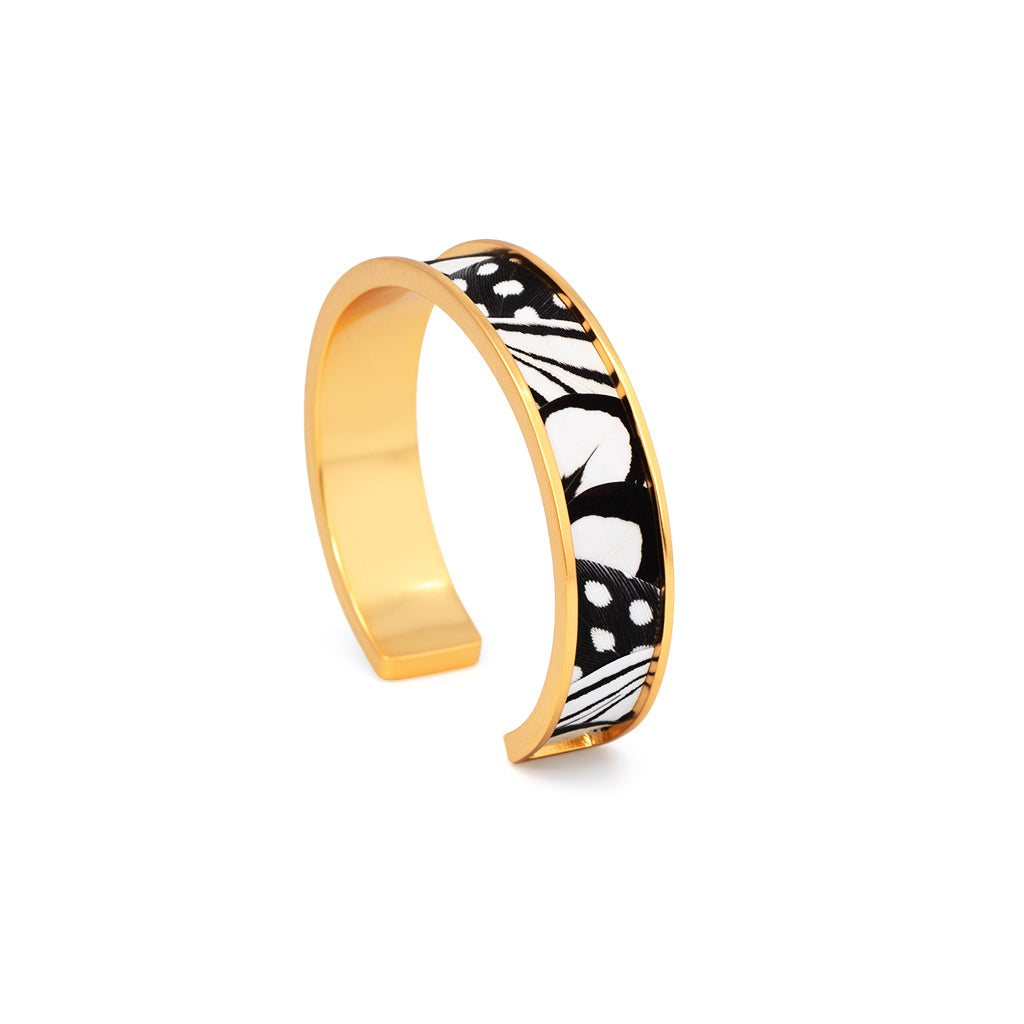 Alternate side view of gold cuff with black and white feather inlay on a white background