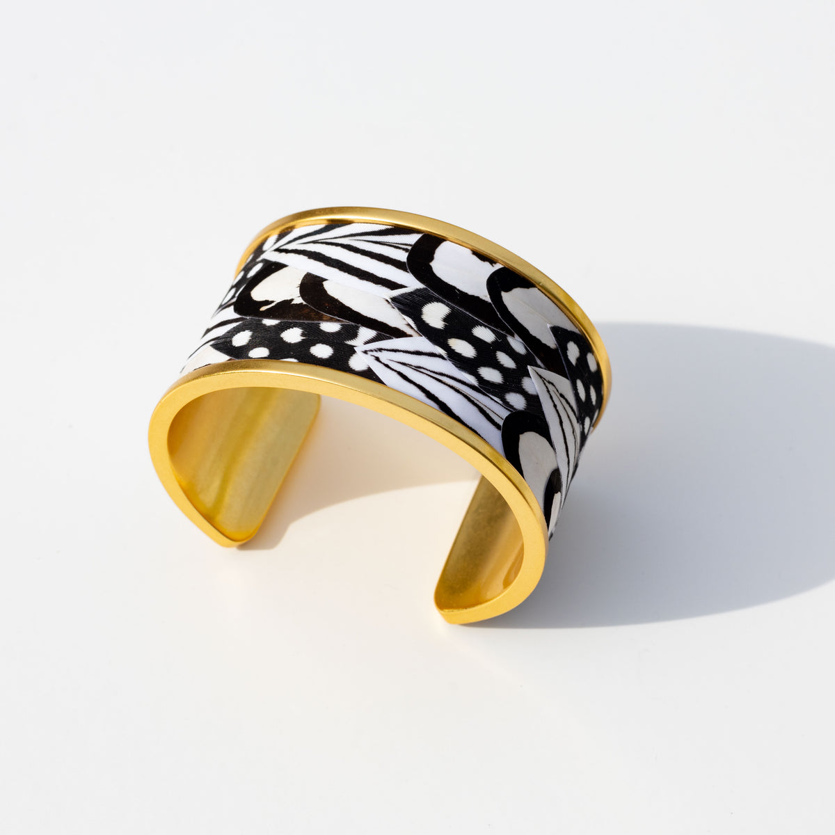 Bottom view of wide gold cuff with black and white feather inlay on a white background