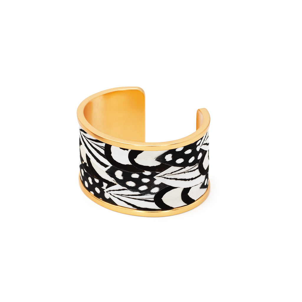Wide gold cuff with black and white feather inlay on a white background
