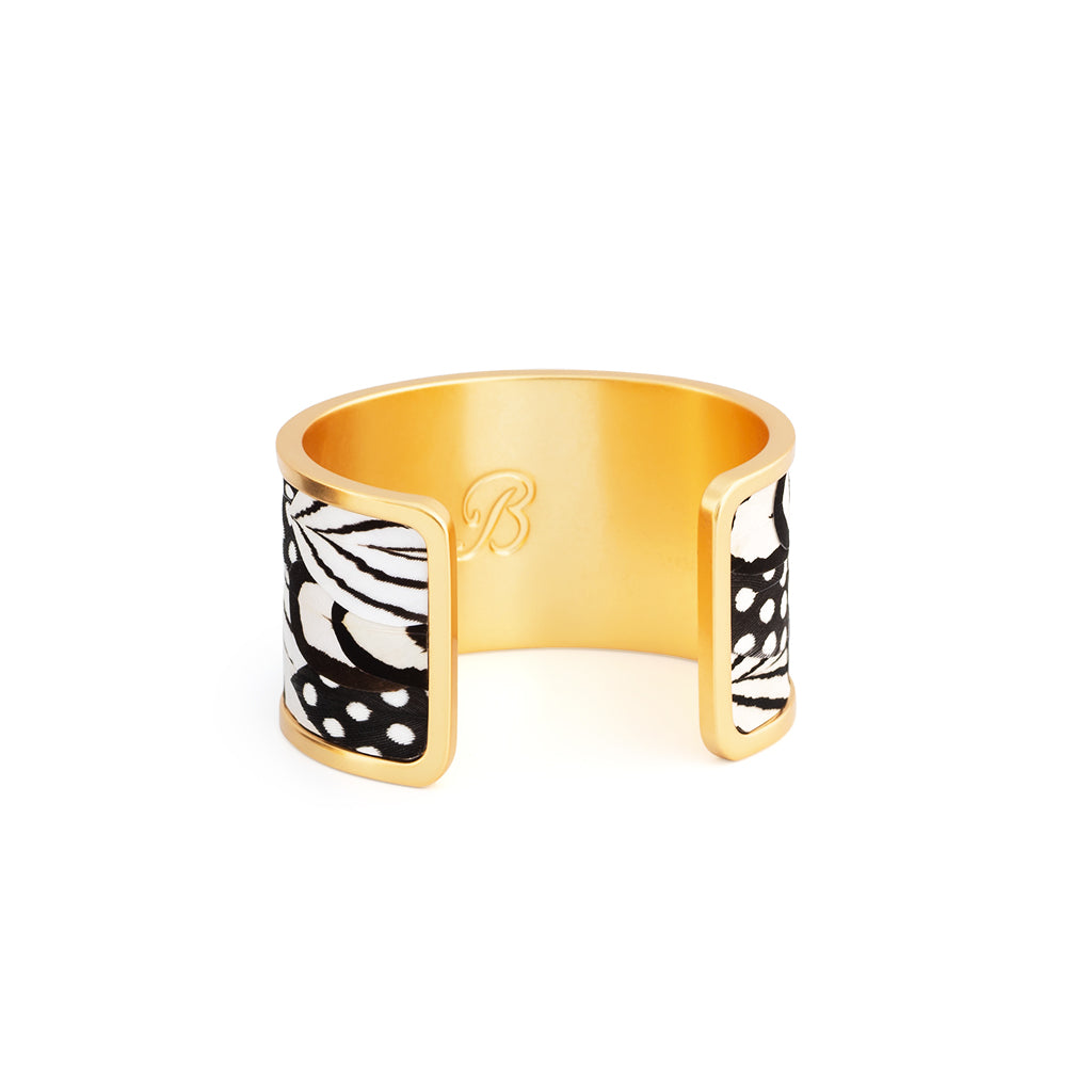 Brackish logo visible on reverse of wide gold cuff with black and white feather inlay on a white background