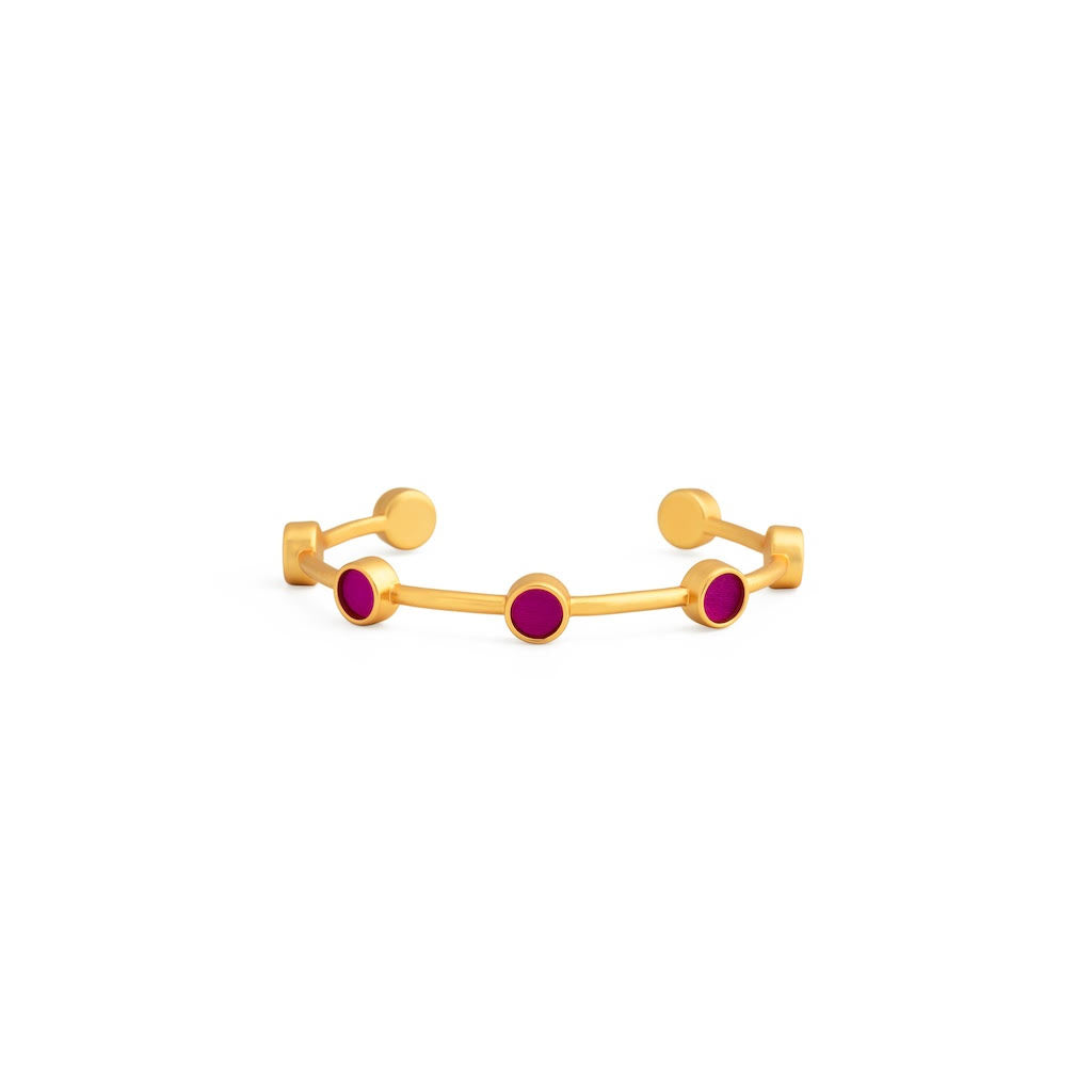 Gold cuff with small round inlays of fuchsia feathers on a white background
