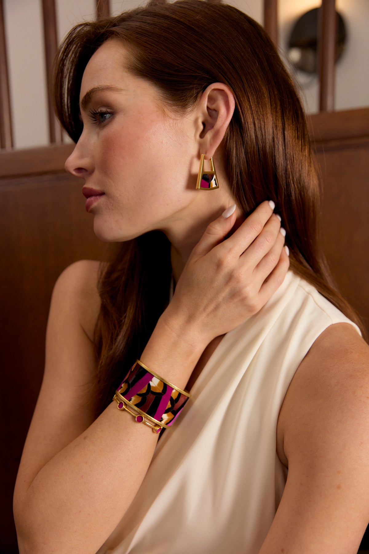 Woman wearing a white dress modeling a gold cuff with small round inlays of fuchsia feathers.