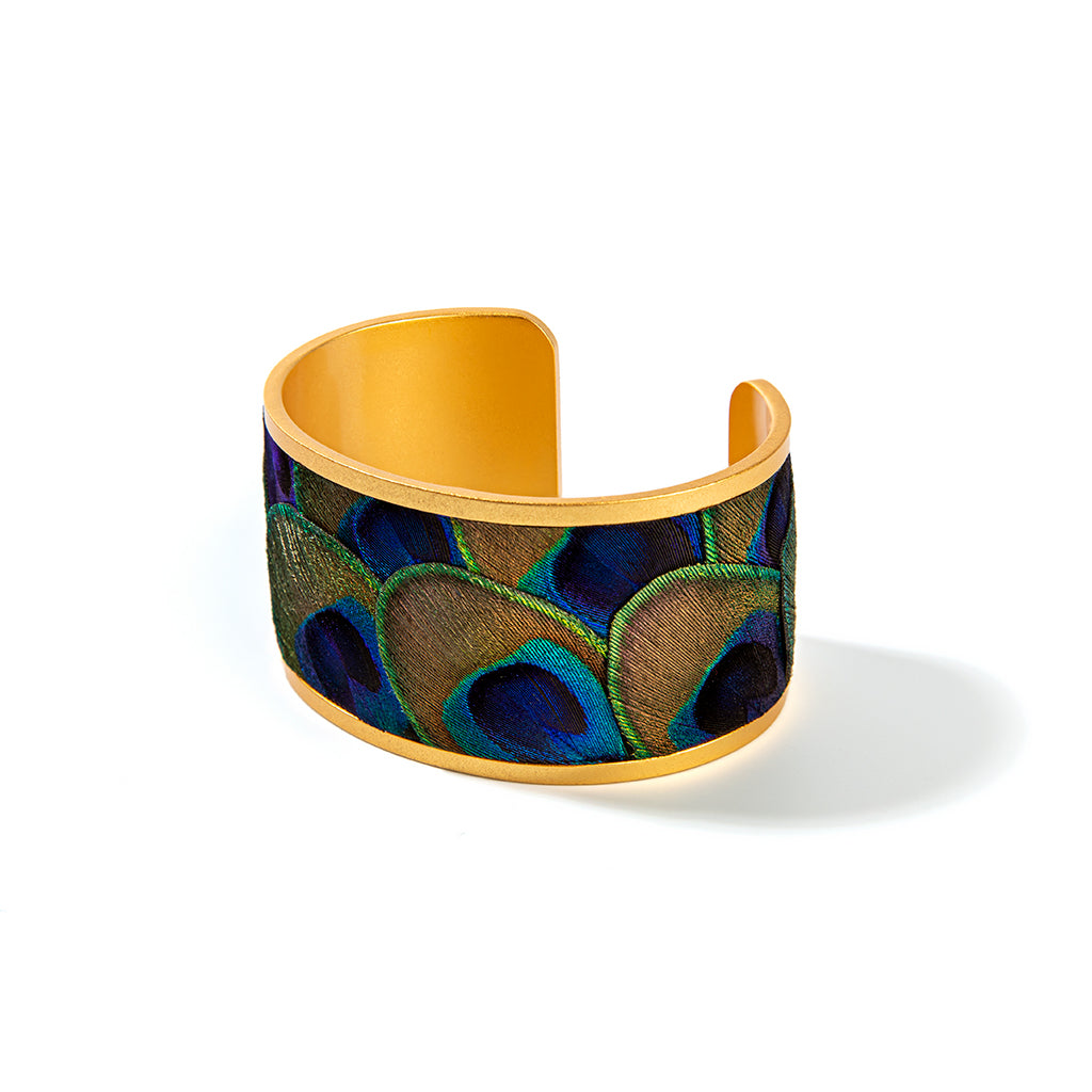 Wide gold cuff with peacock feather inlay on a white background