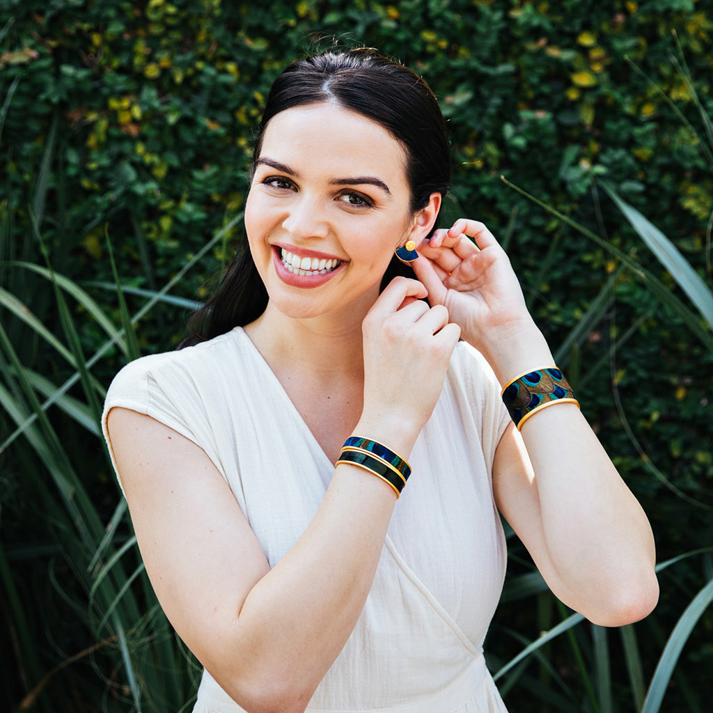Woman in a white dress modeling wide gold cuff with peacock feather inlay