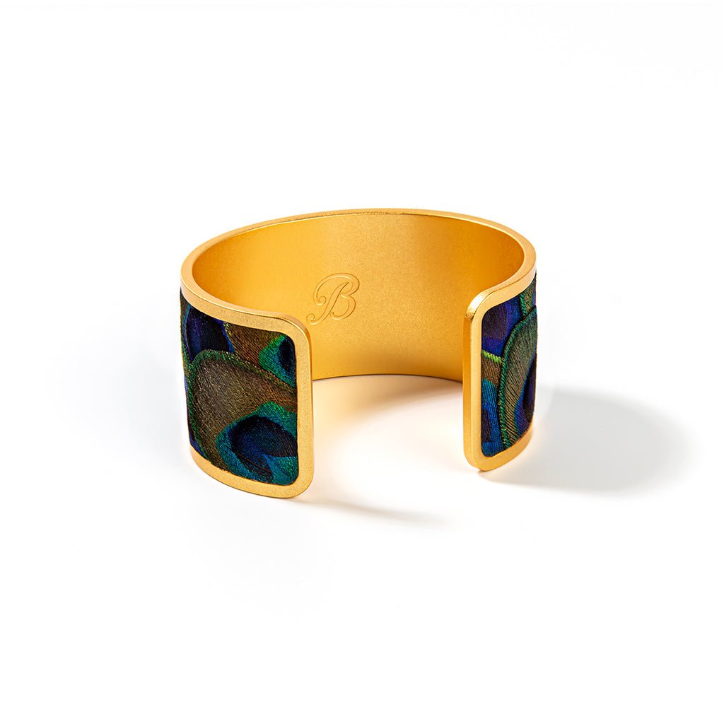 Brackish logo visible on reverse of wide gold cuff with peacock feather inlay on a white background