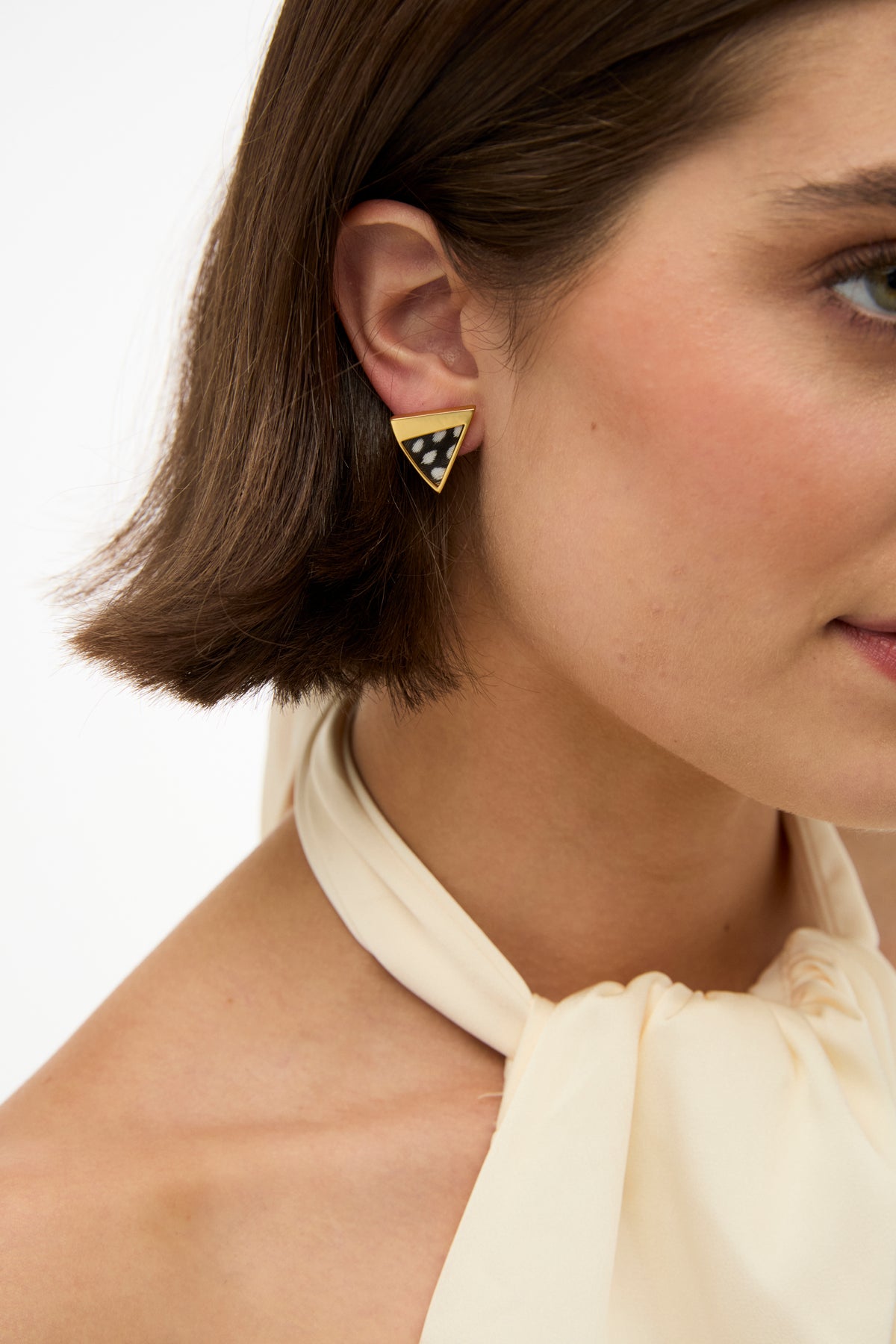 Close-up of a woman wearing a gold earring with a checkered design on a plain background