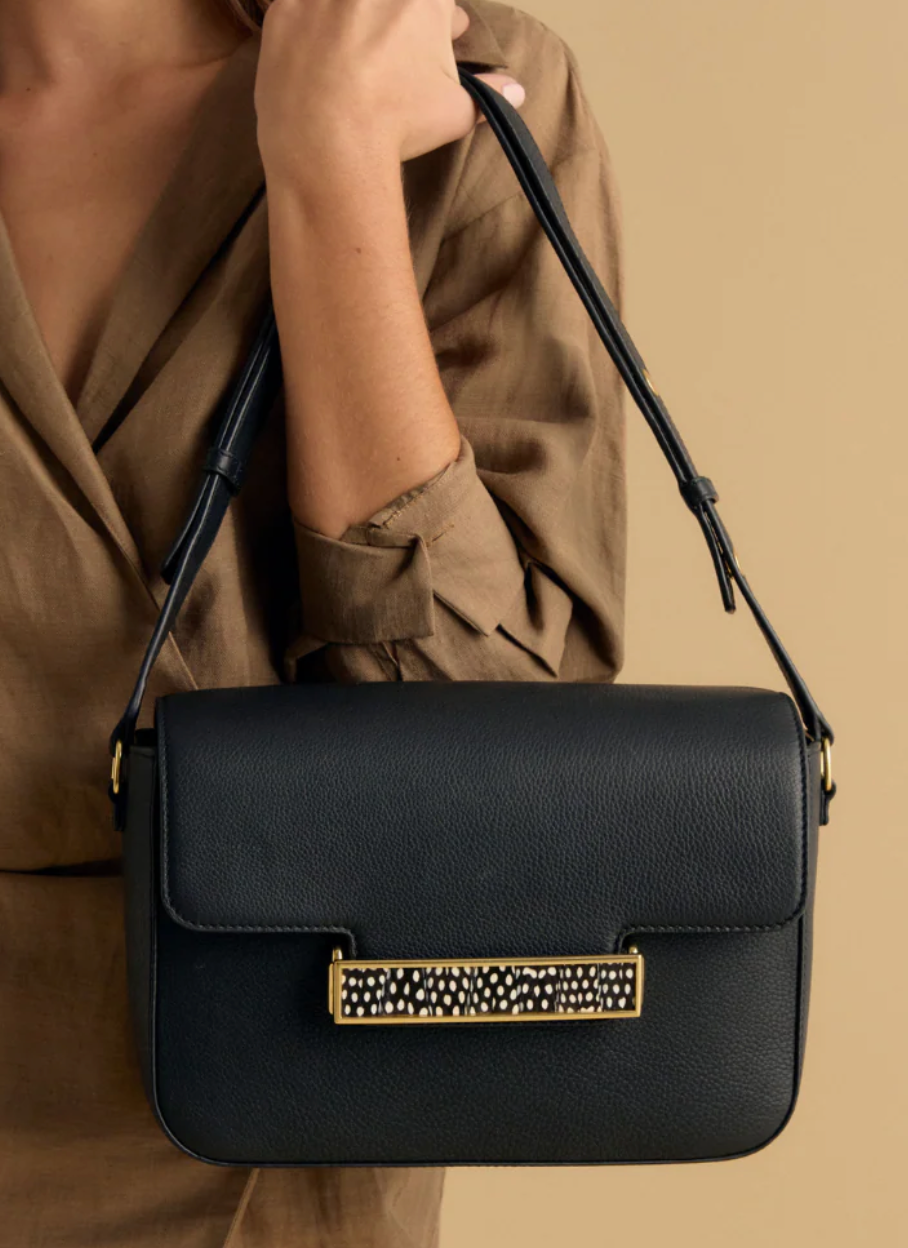 Woman in a brown dress modeling a black leather handbag with gold clasp featuring black and white feather inlay