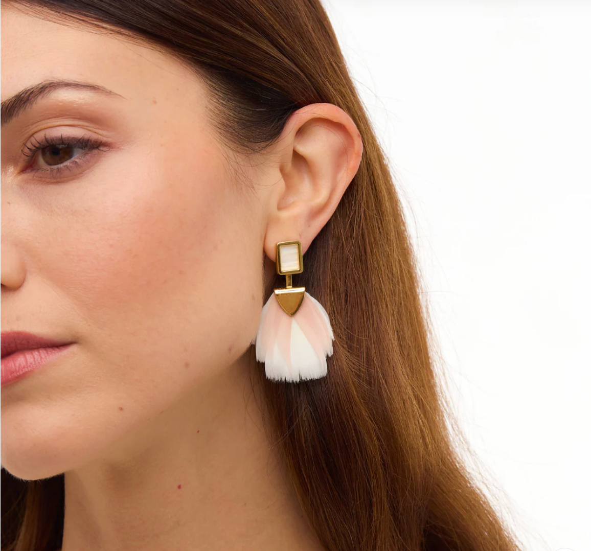Close-up of a woman wearing a gold earring with pink and white feather tassels against a white background