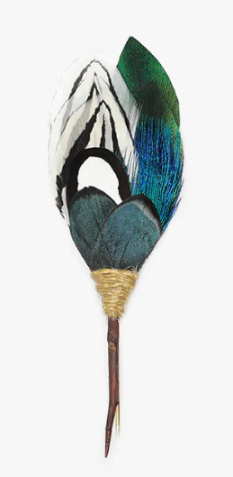 Lapel pin made of blue, green, and white feathers attached to a thorn on a white background