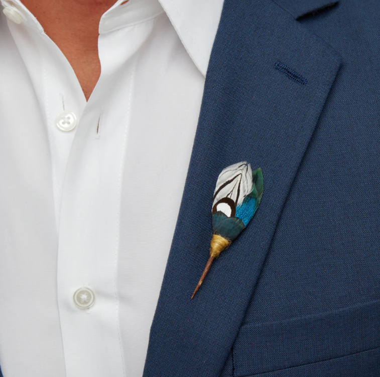 A blue, green and white feather lapel pin modeled on a navy blazer.