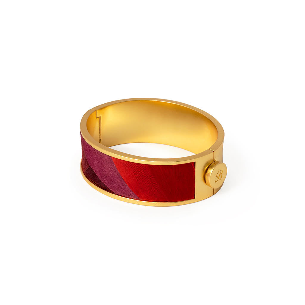 Gold hinged cuff with inlay of red and purple feathers on a white background