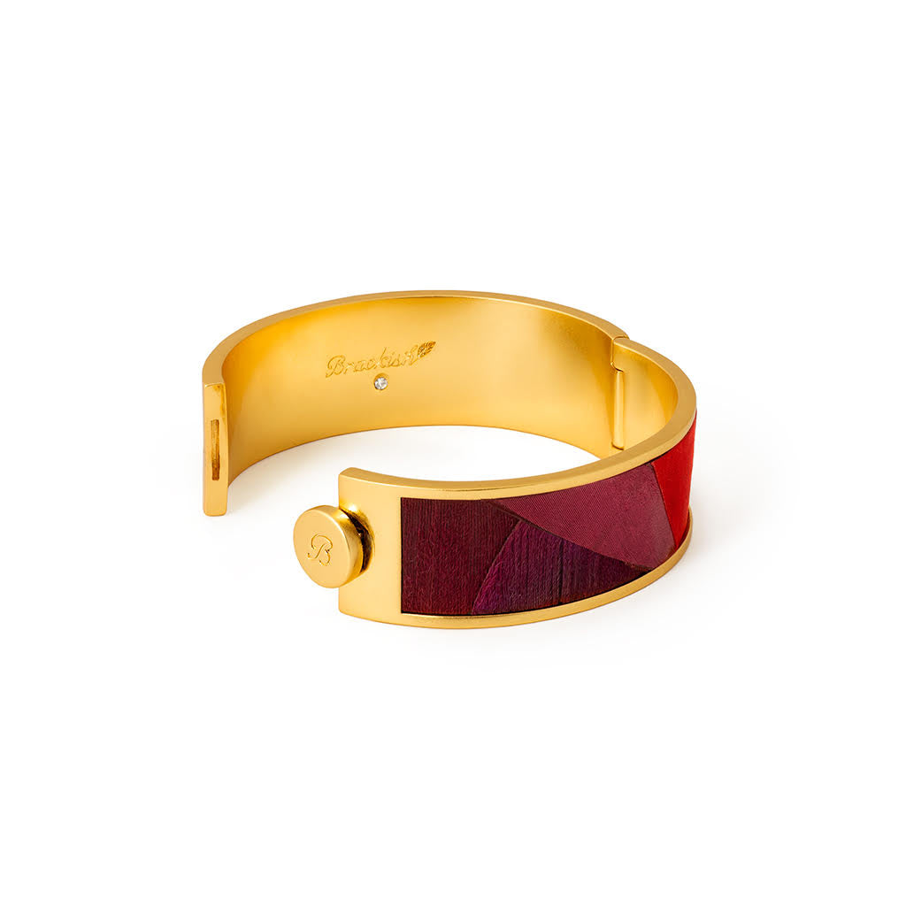 Gold hinged cuff with inlay of red and purple feathers open with Brackish logo visible on inside of cuff against a white background