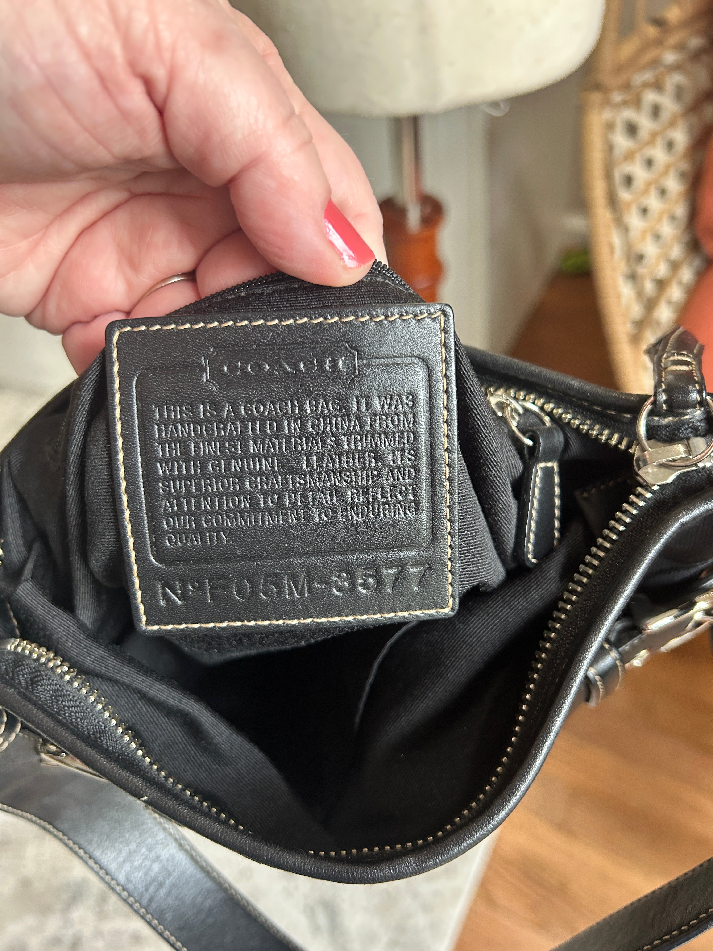 Coach Black leather handbag with a Creed held by a hand.