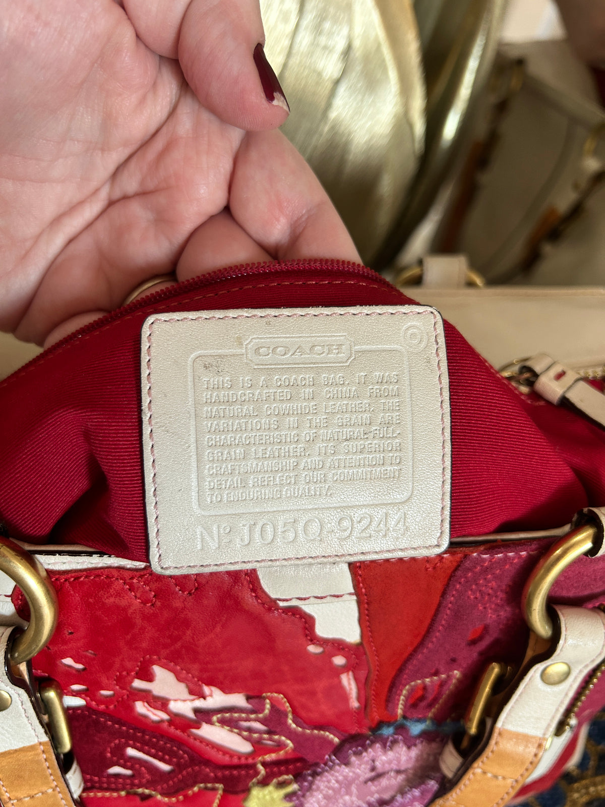 Close-up of a Coach handbag interior showing a red fabric lining with a cream colored leather brand patch and part of a multicolored exterior pattern.