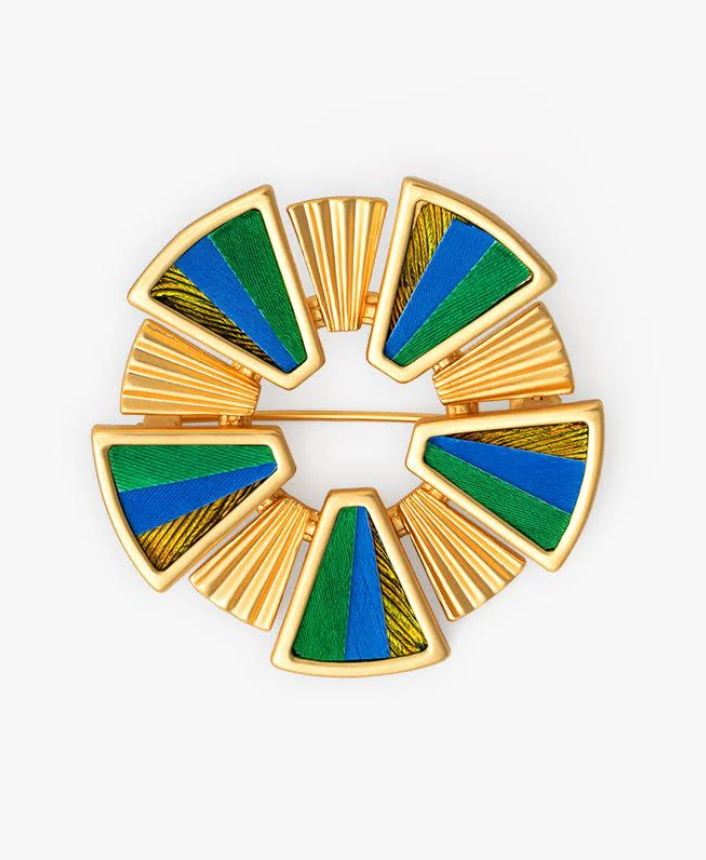 Decorative circular gold brooch with green and blue feather inlay design on a white background