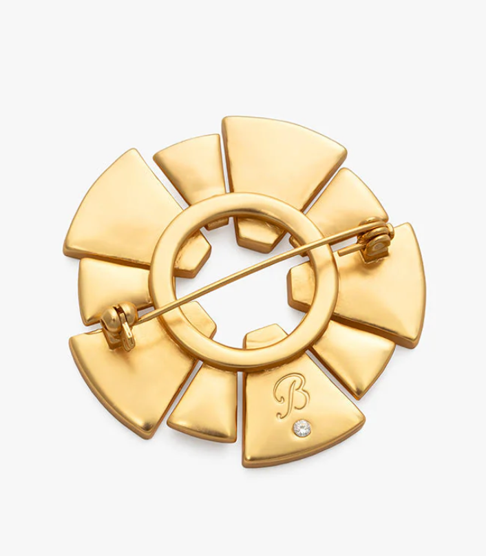 Gold brooch with a central circular design on a white background