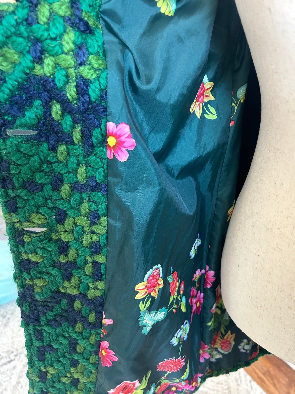 Close-up of a garment on a mannequin, showing a textured green and navy  knit panel alongside a dark teal lining with colorful floral print.