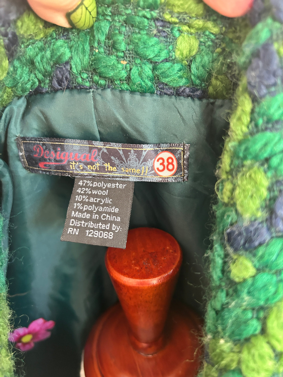 Close-up of a green textured knit garment interior showing a sewn-in size 38 label with fabric composition details and a dark green satin lining.