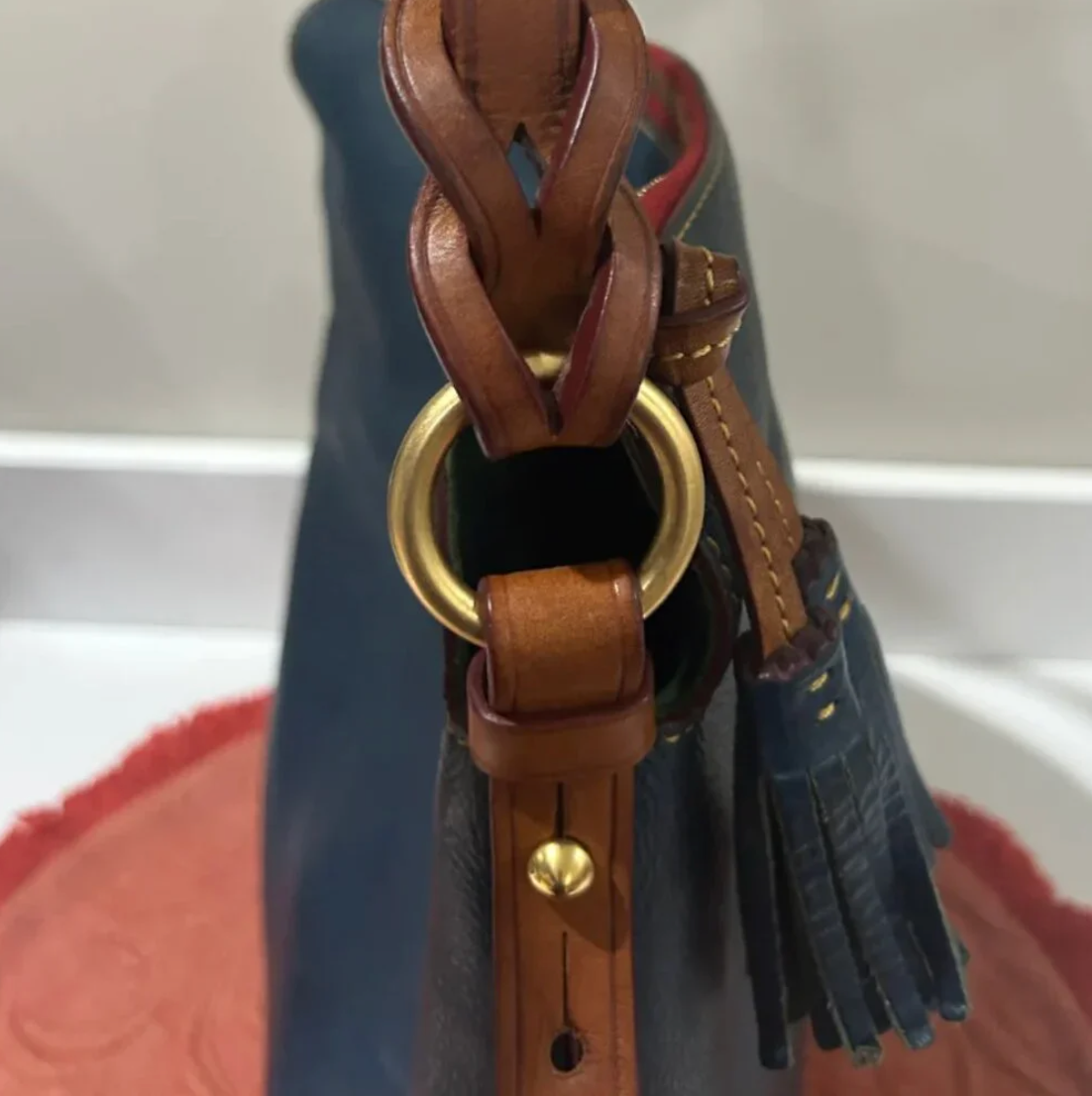 Close-up of a brown leather strap with a gold ring on a blue leather bag