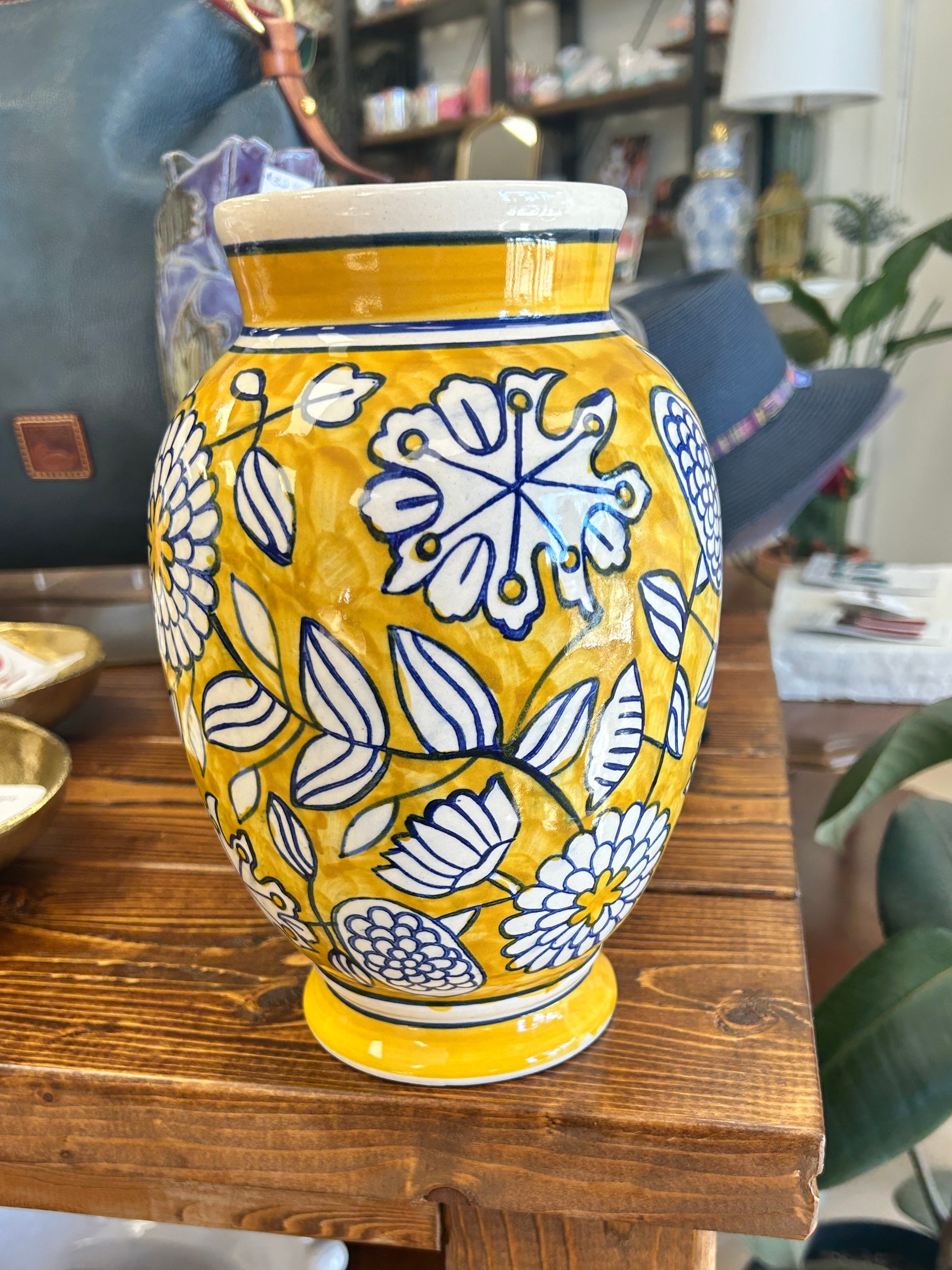 Decorative chinoiserie style yellow vase with floral patterns on a wooden shelf.