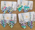 Colorful leaf-shaped earrings on branded cards displayed on a wooden surface.
