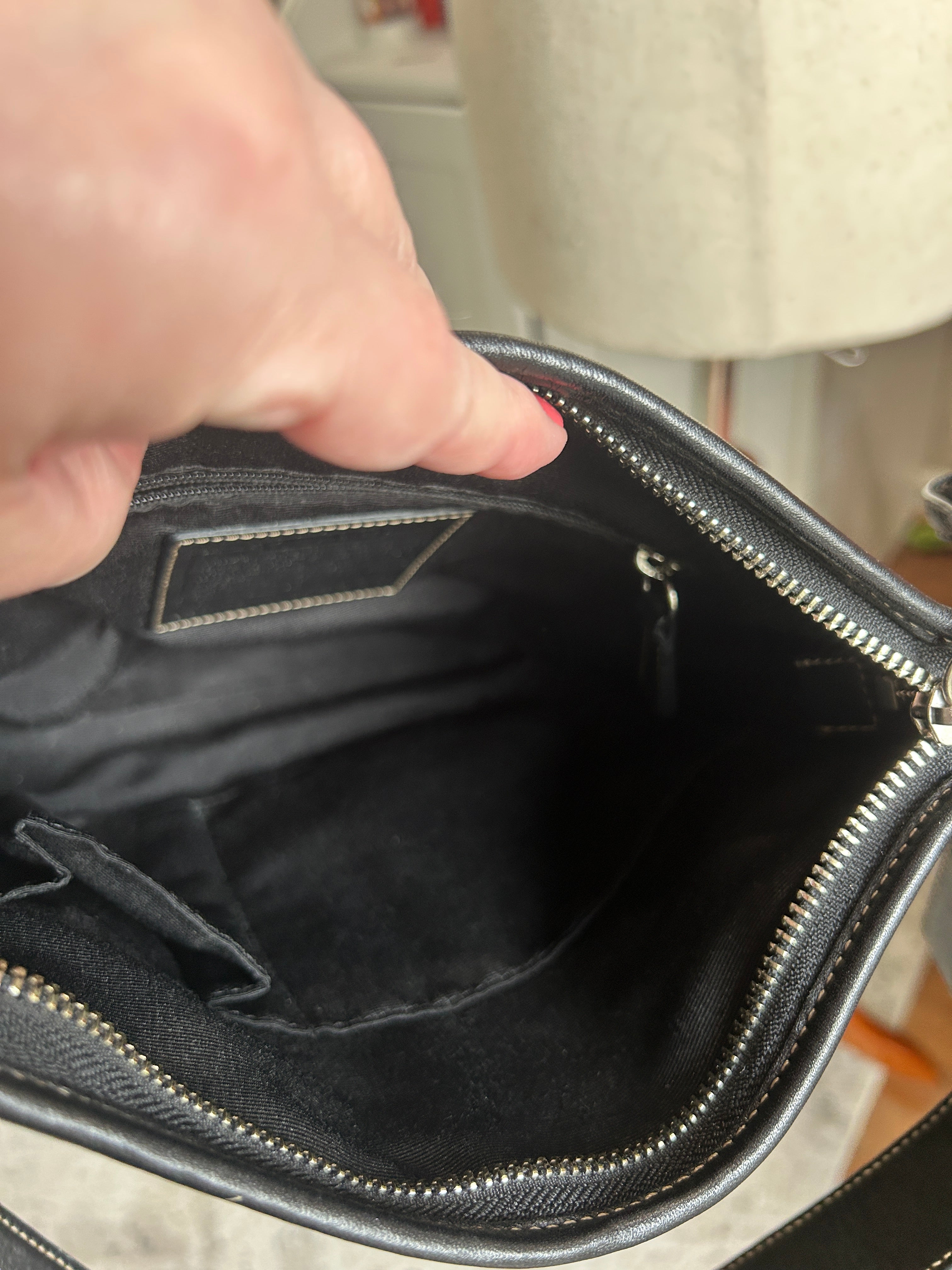 Hand opening a black leather bag with a visible brand label.