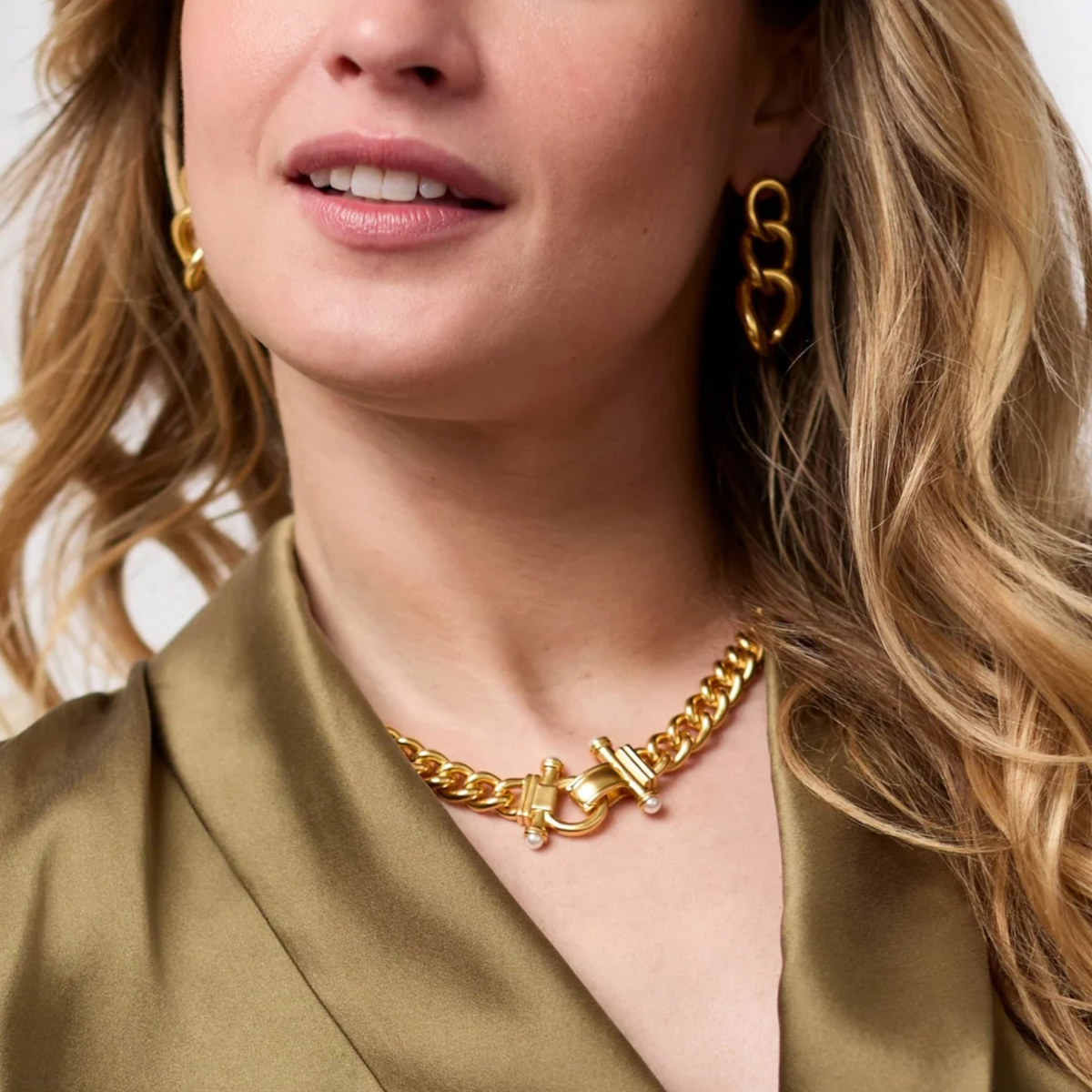 A woman wearing a gold chain link necklace with ornate clasp with pearls and matching earrings