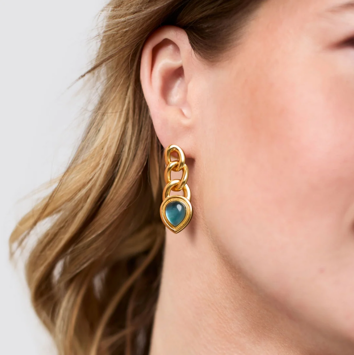 A woman is wearing a gold chain link earring with a blue stone