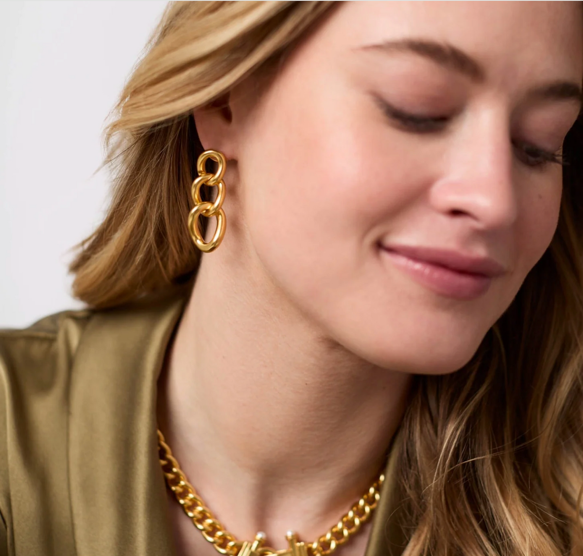 A woman is wearing a gold chain link earring and matching necklace