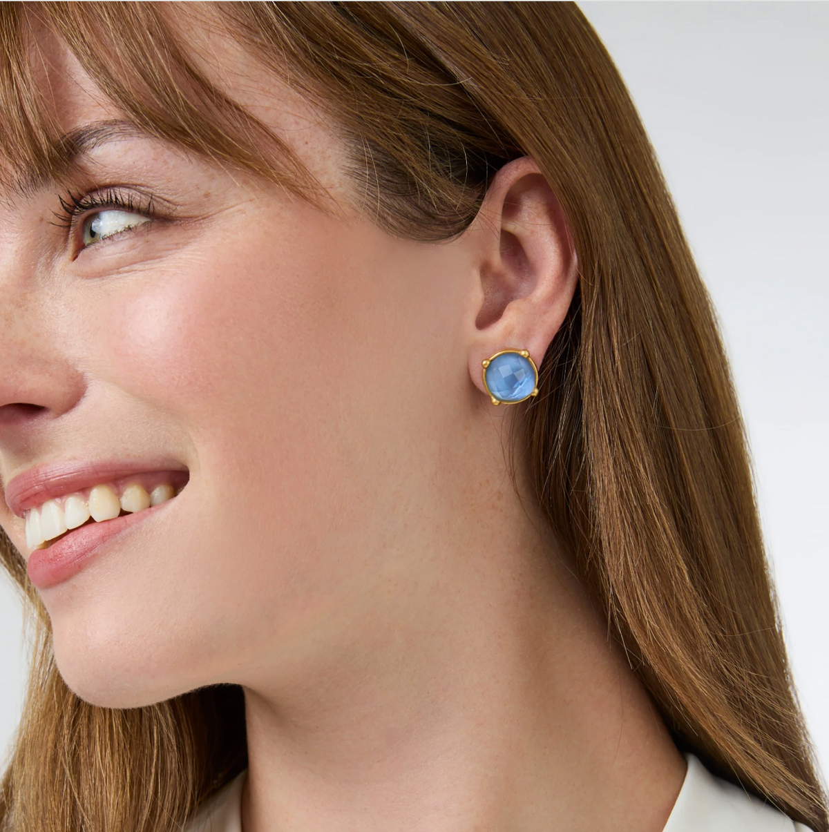 A woman is wearing a gold stud with a blue stone