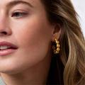 A woman wearing gold hoops with domed ball shapes