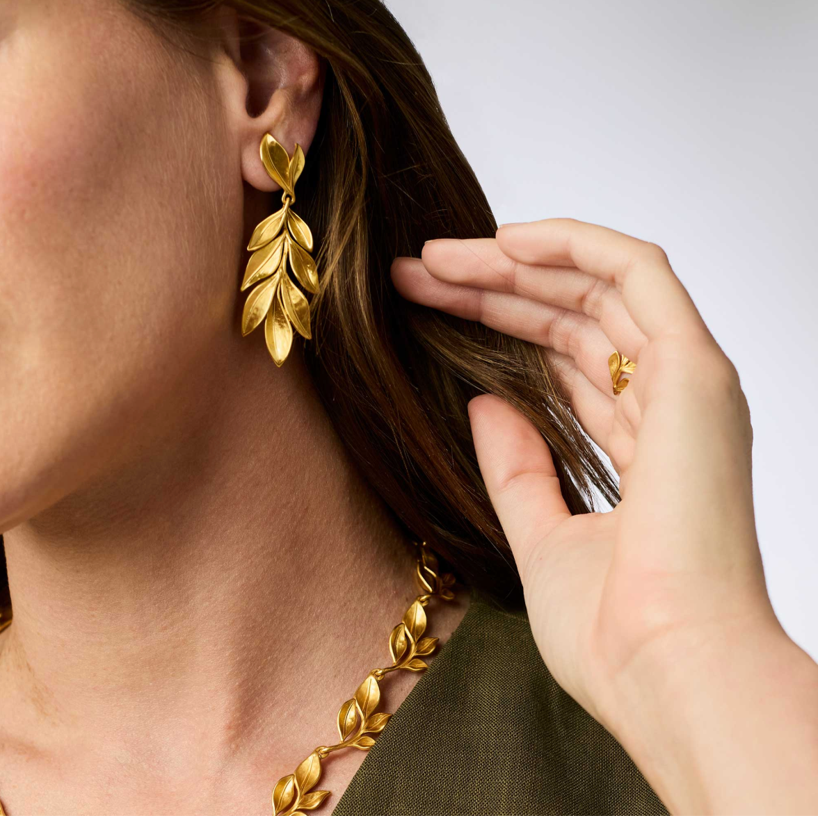 A woman wearing a long gold earring with leaves and matching necklace
