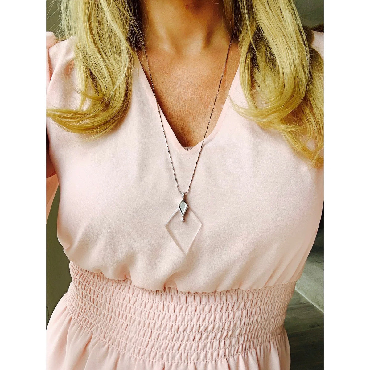 Woman in a light pink dress wearing a silver necklace with a diamond-shaped monocle pendant.