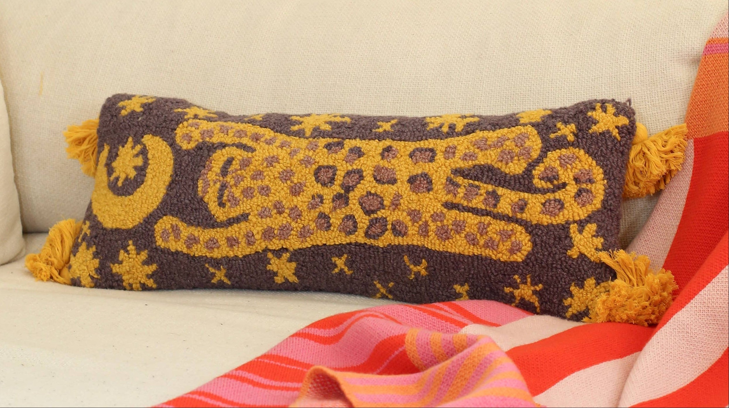 A decorative pillow with a leopard print design on a sofa, with a tassel on each corner. The pillow is primarily brown with black spots, set against a light background.