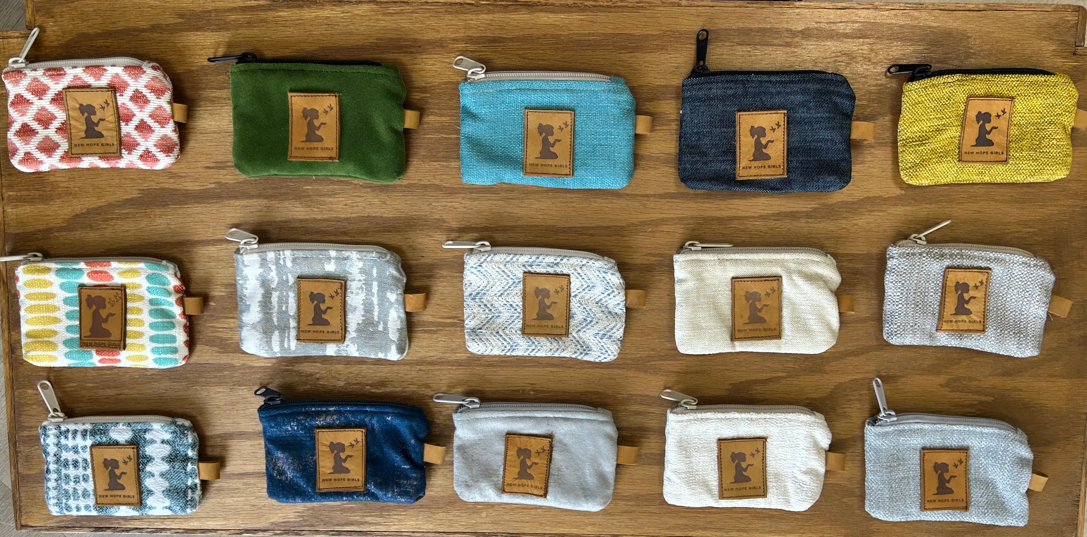 Collection of colorful coin pouches with New Hope Girls leather brand logo on a wooden surface