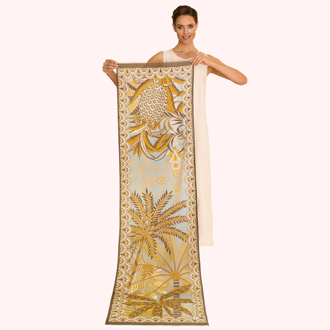 Woman holding a long, decorative scarf with yellow and brown palm tree design on a white background